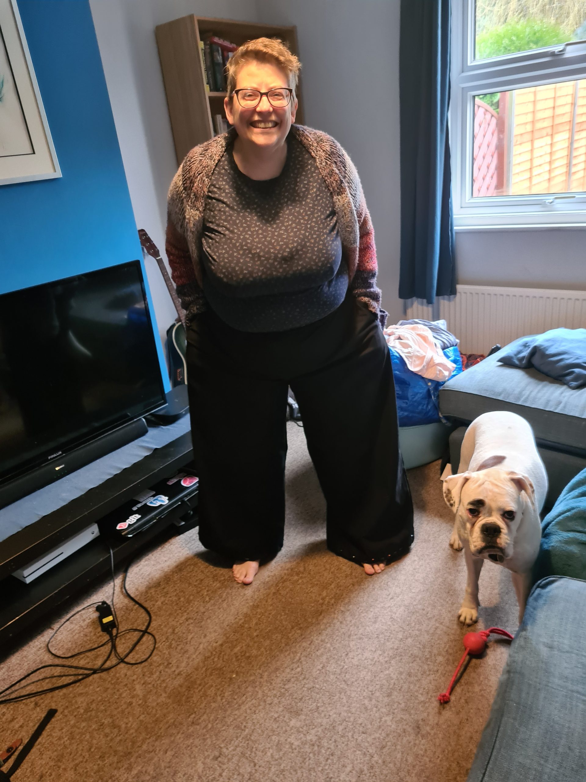 woman wearing black trousers with pockets. white boxer dog in foreground